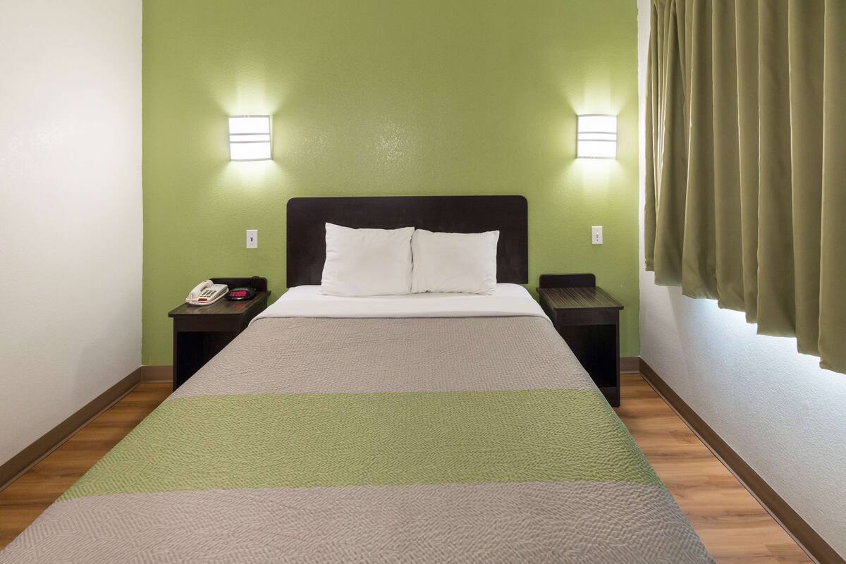 Une chambre d’hôtel comprenant un lit, deux tables de chevet, un téléphone et deux lampes fixées au mur.