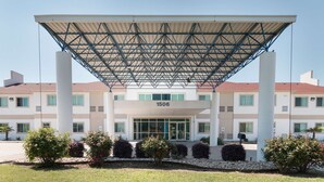 A hotel entrance with a covered entrance canopy, numbered 1506, and a landscaped garden area with shrubs and flowers. - Motel 6 Hillsboro, TX (Hillsboro)