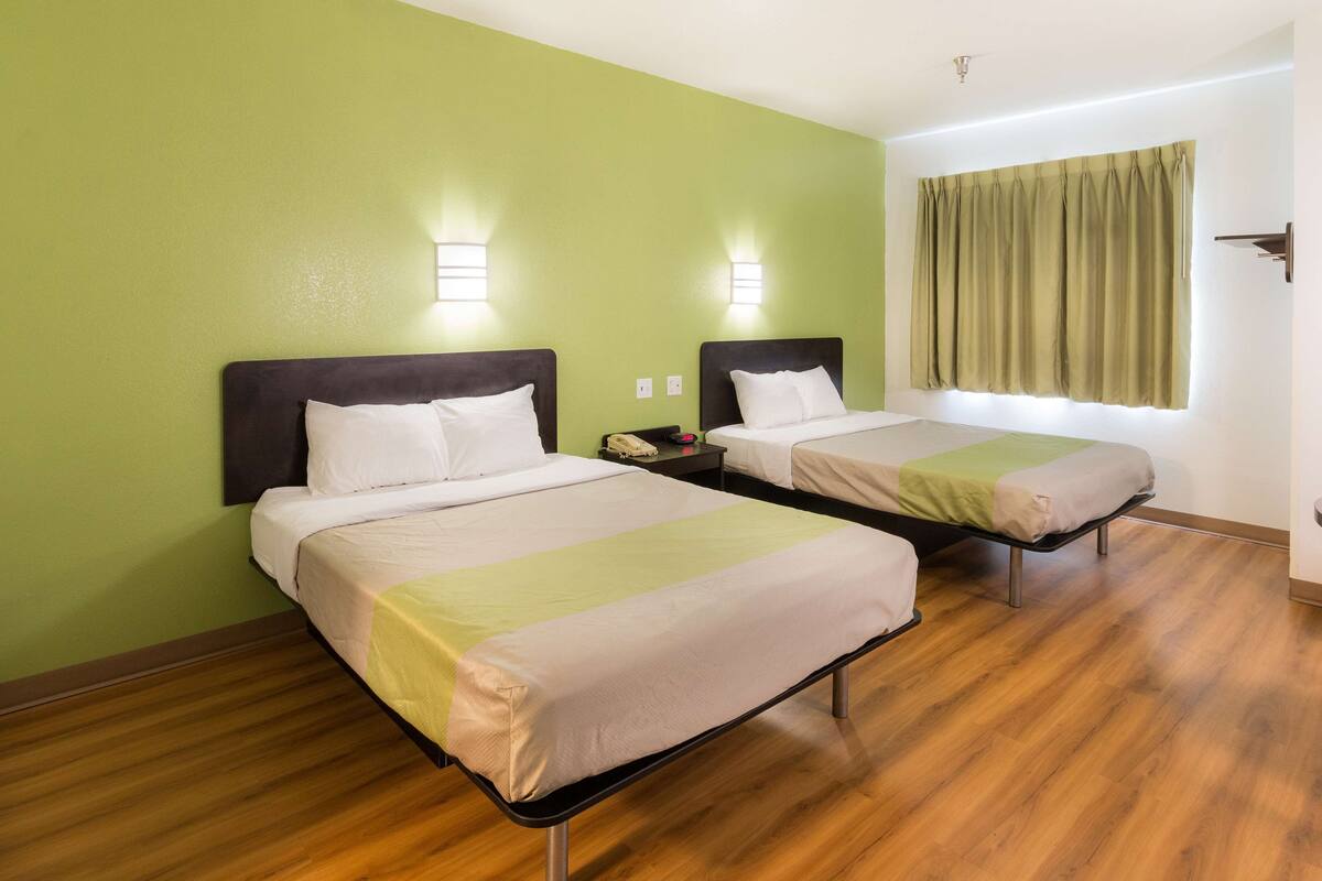 Une chambre d’hôtel avec deux lits, un plancher en bois, des murs verts et des lampes de chevet.