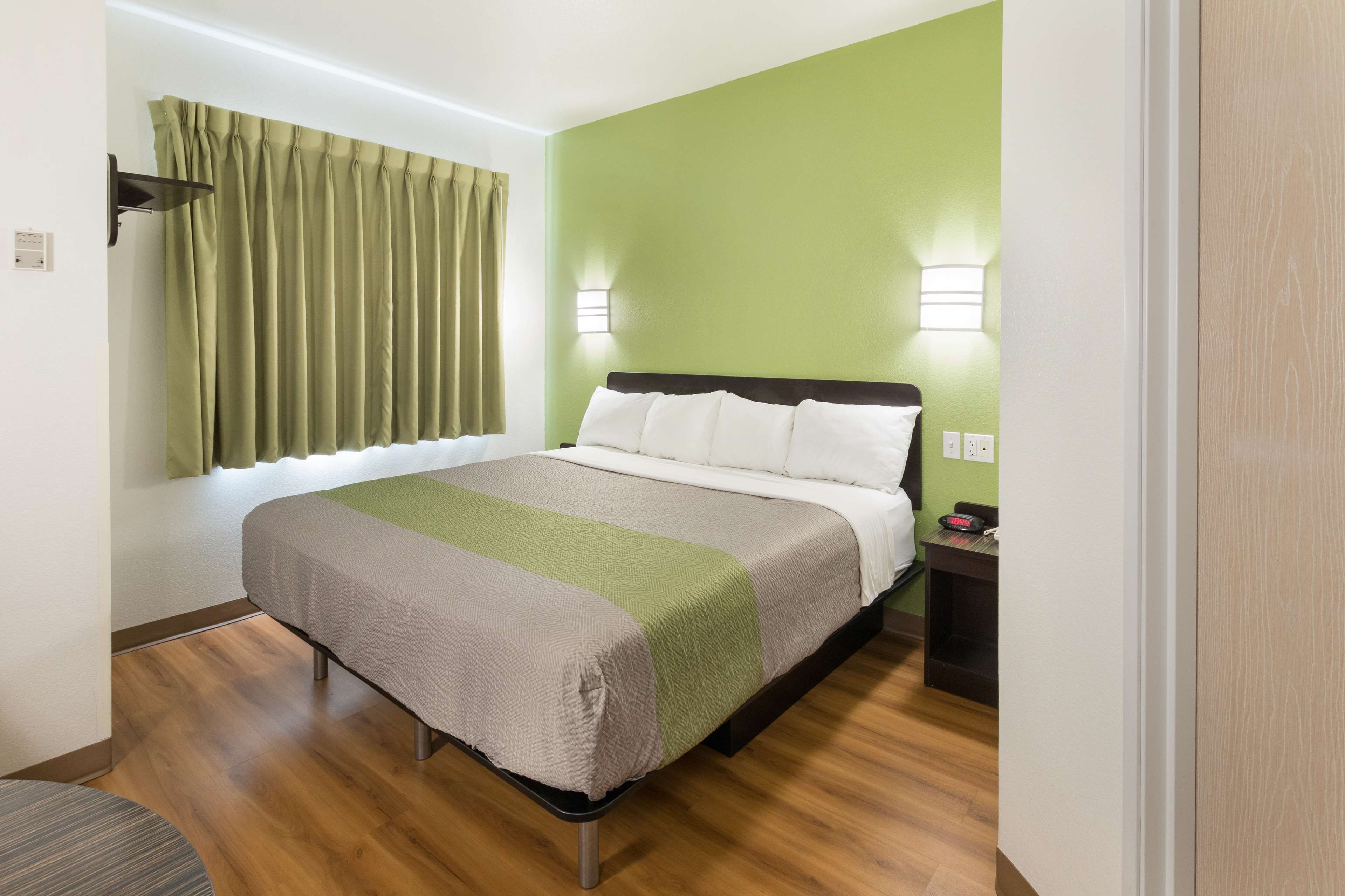 Uma cama bem arrumada com um edredom listrado, uma mesa de cabeceira com abajur e uma janela com cortinas.