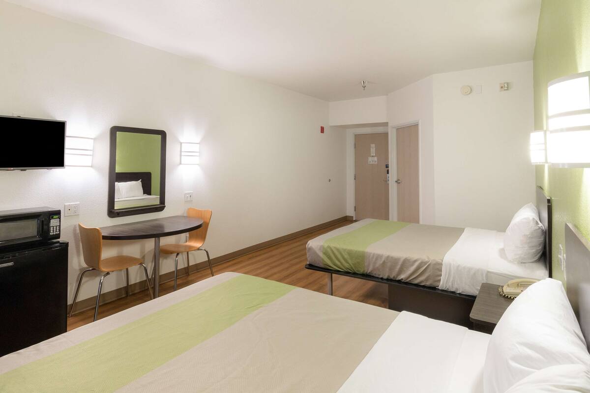 Une chambre d’hôtel avec deux lits, un bureau avec une chaise, une télévision et un four à micro-ondes.