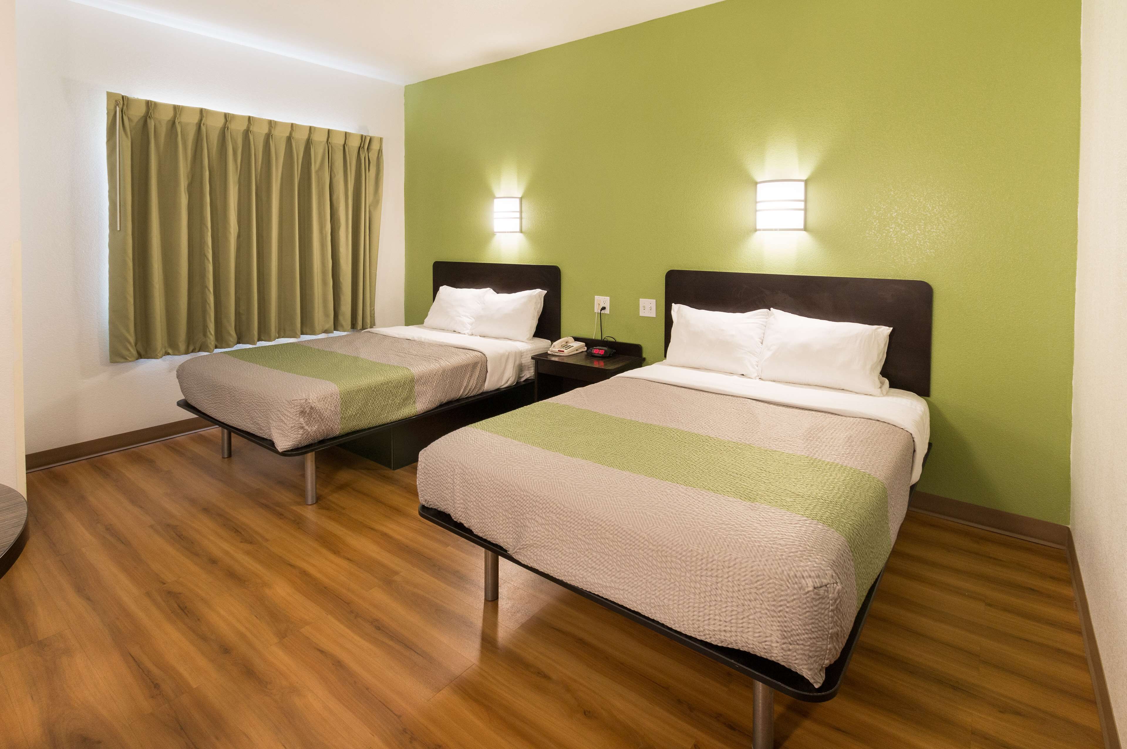 A hotel room with two beds, wooden flooring, green walls, and bedside lamps.