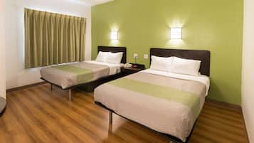 A hotel room with two beds, wooden flooring, green walls, and bedside lamps.