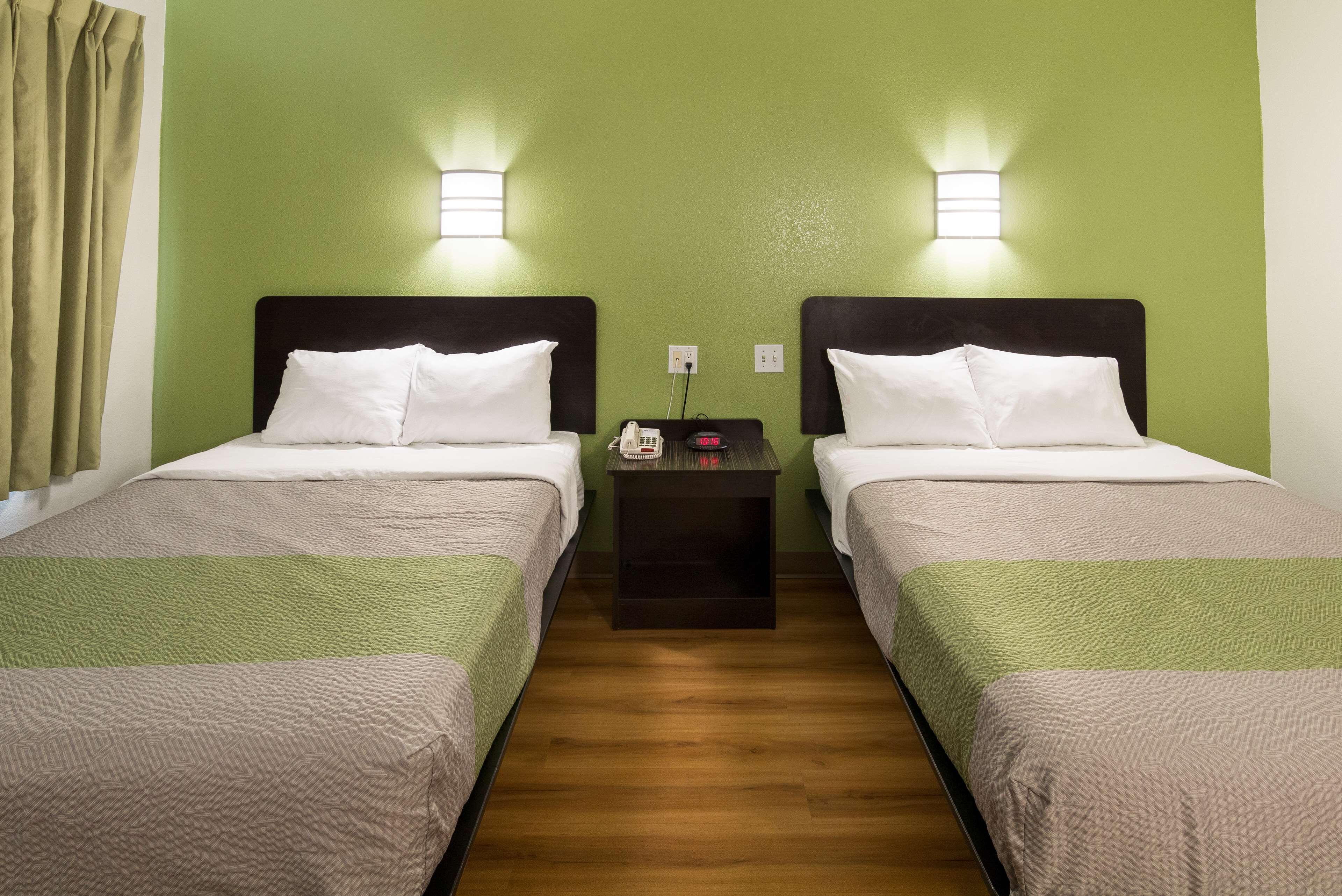 A hotel room with two beds, each with a headboard, a nightstand between them, and a wall-mounted phone.