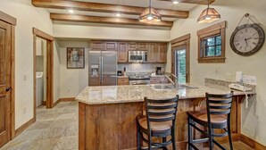 A kitchen with wooden beams, granite countertops, stainless steel appliances, and a large island with bar stools.