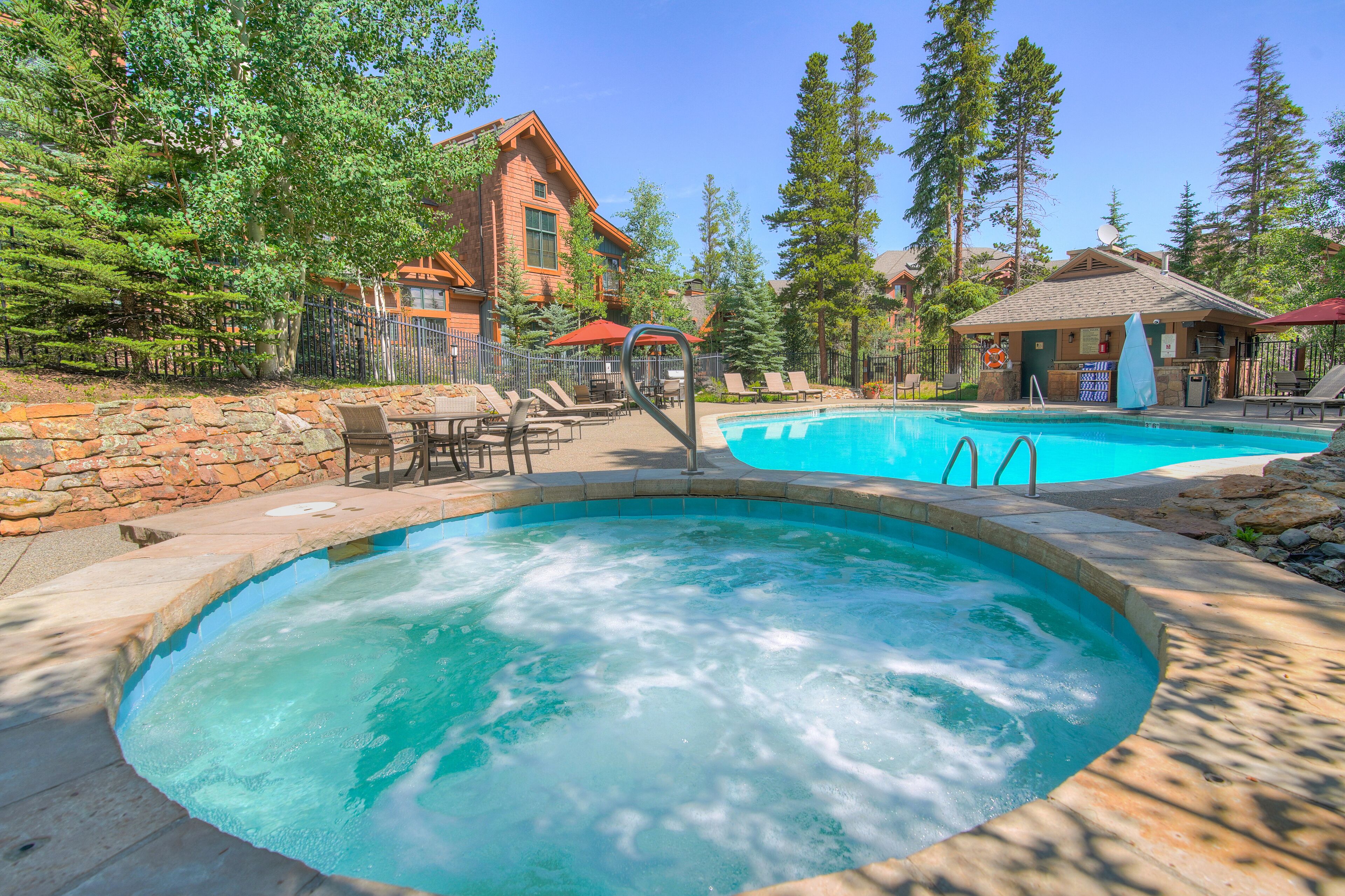 A hot tub and a pool area with lounge chairs and a stone wall.