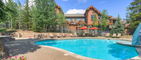 A pool area with lounge chairs and a building with a wooden facade in the background.