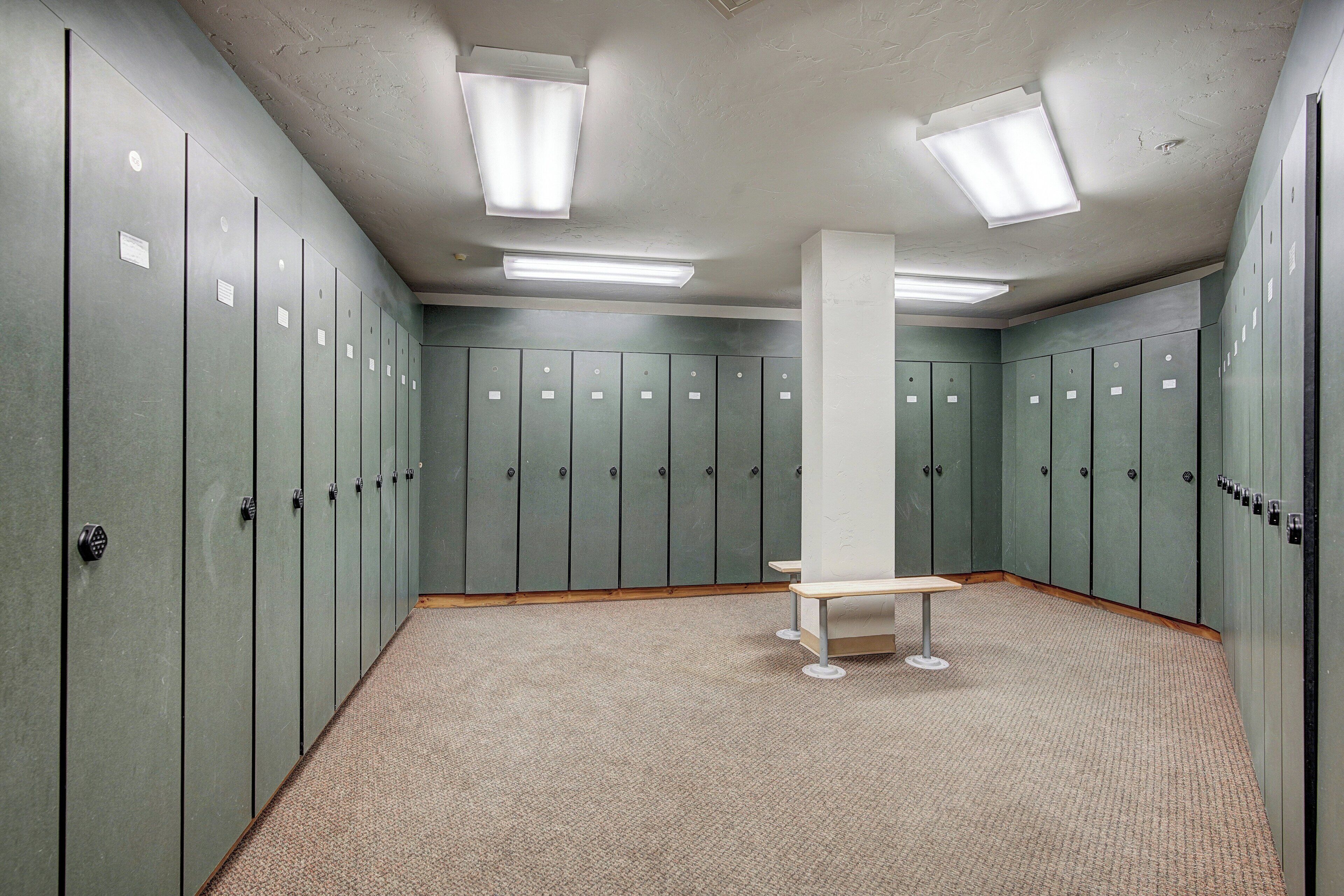 A locker room with multiple lockers, a bench, and fluorescent lighting.