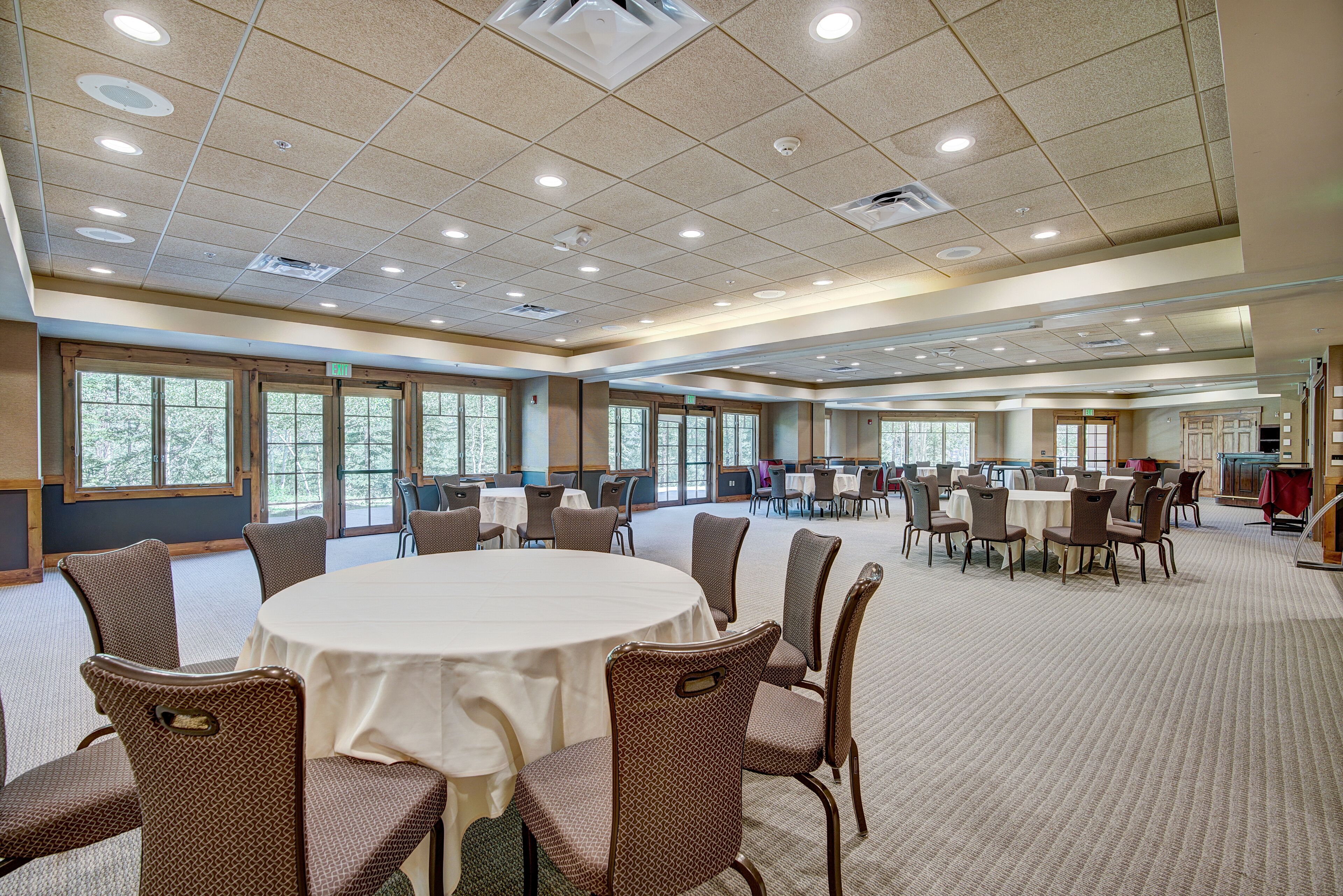 A large conference room with round tables and chairs, large windows, and a carpeted floor.