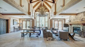 A spacious living area with a high ceiling, wooden beams, a fireplace, and a large chandelier.