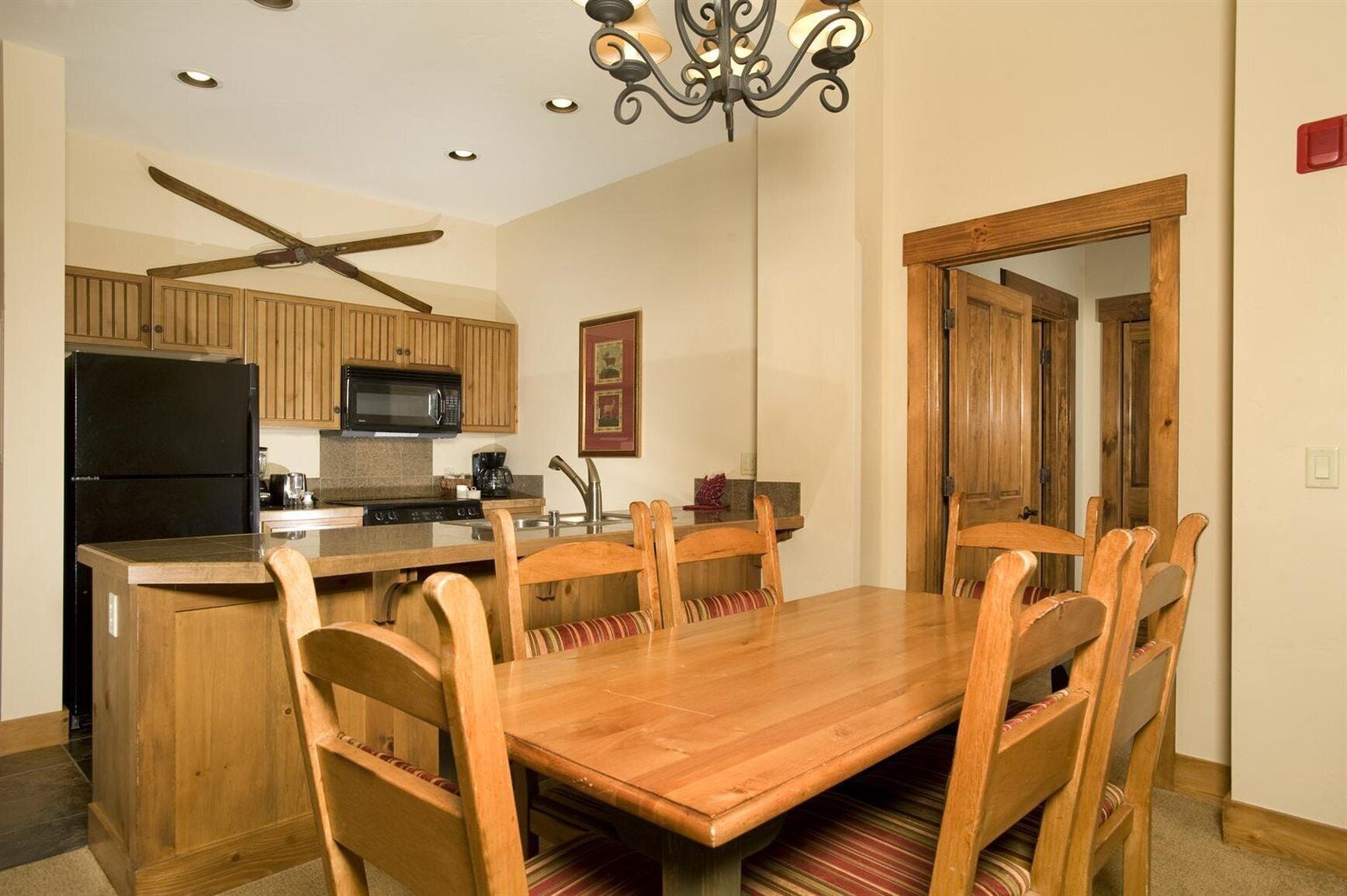 A kitchen with wooden cabinets, a black refrigerator, a microwave, and a dining area with a wooden table and chairs.