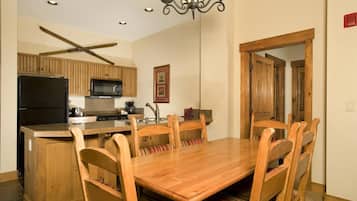 Una cocina con armarios de madera, un refrigerador negro, un microondas y un comedor con una mesa y sillas de madera.