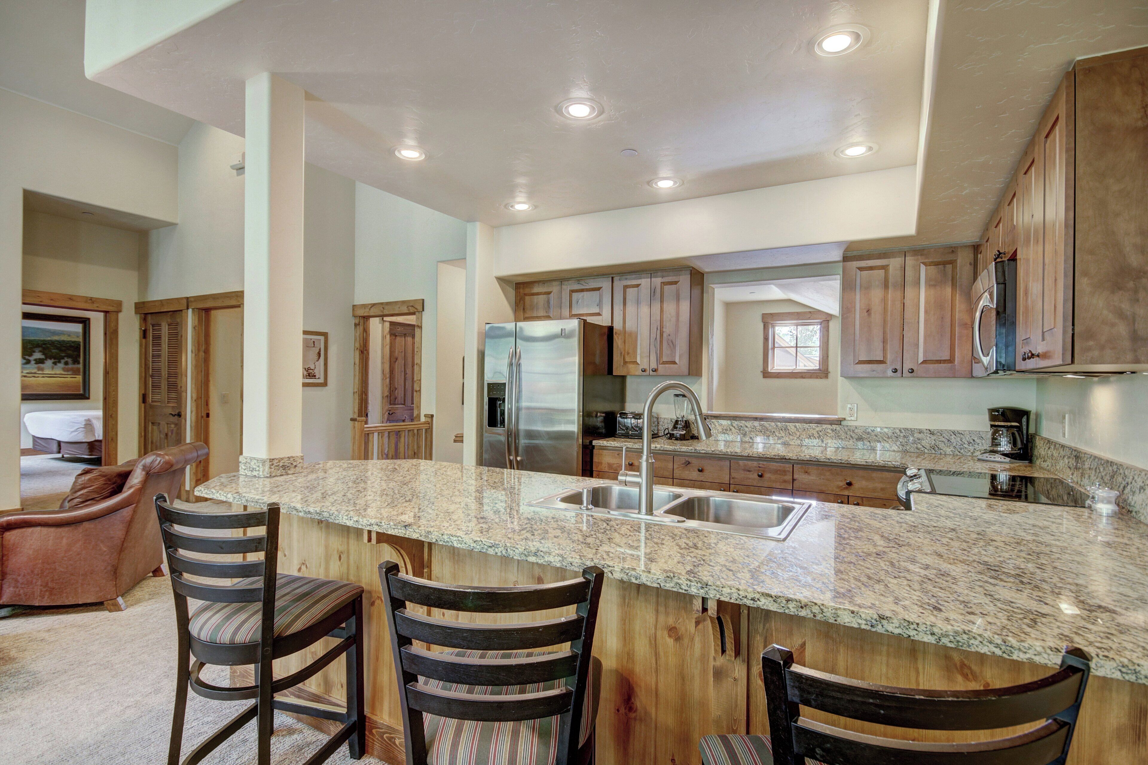 A kitchen with granite countertops, wooden cabinets, and a central island with bar stools.