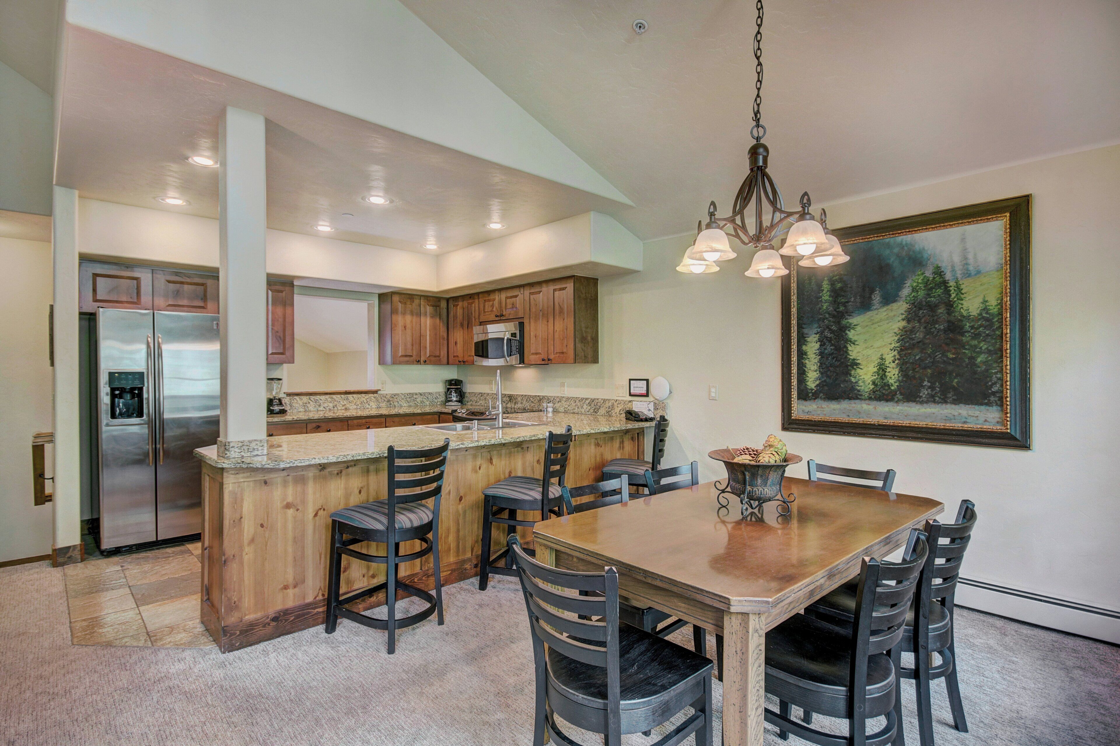 Una cocina con isla central, armarios de madera, electrodomésticos de acero inoxidable y una zona de comedor con mesa y sillas de madera.
