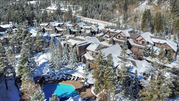 A snow-covered resort with multiple buildings, a swimming pool, and a ski slope in the background.