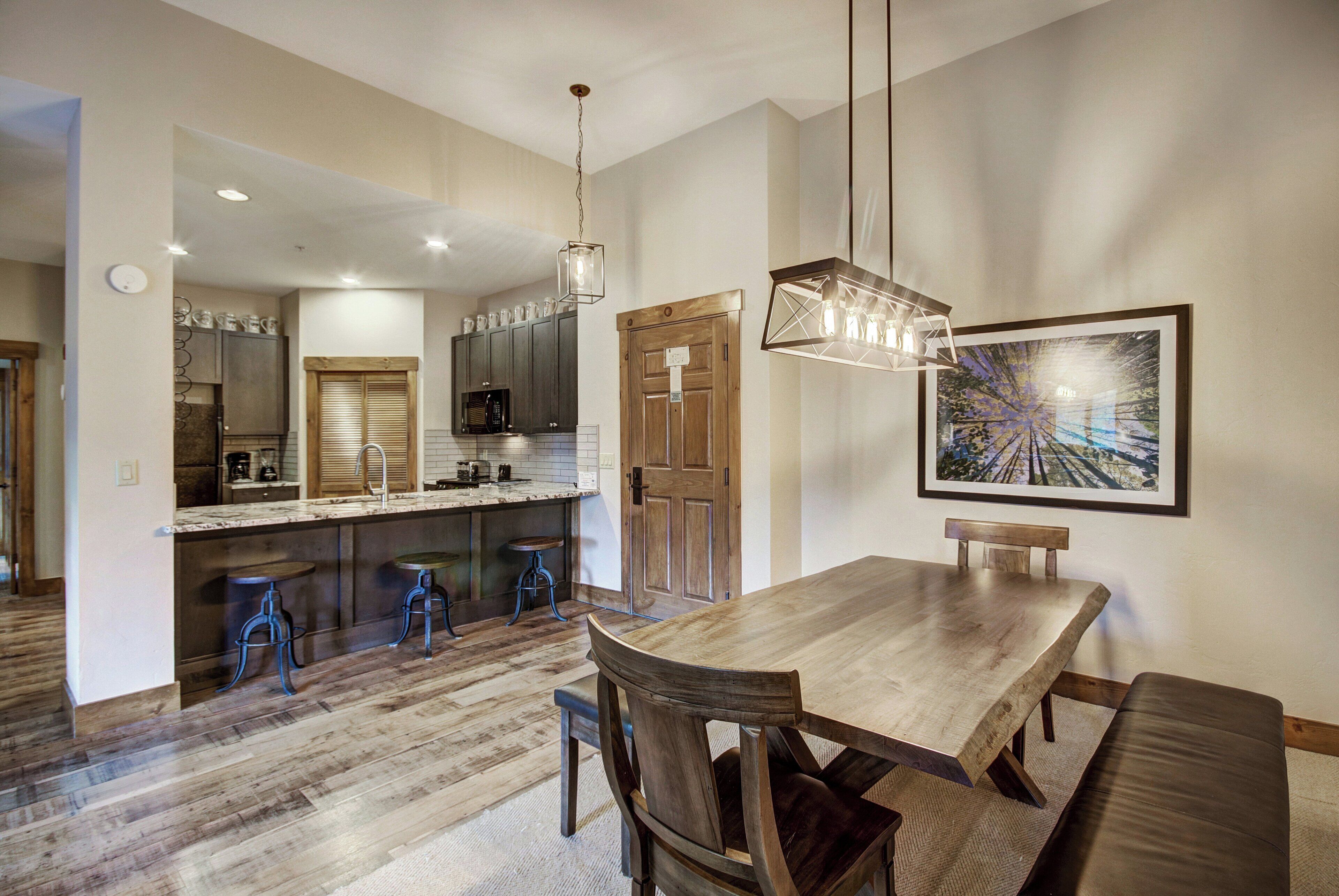 A modern kitchen with dark cabinets, a wooden dining table, and bar stools.
