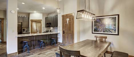 A modern kitchen with dark cabinets, a wooden dining table, and bar stools.