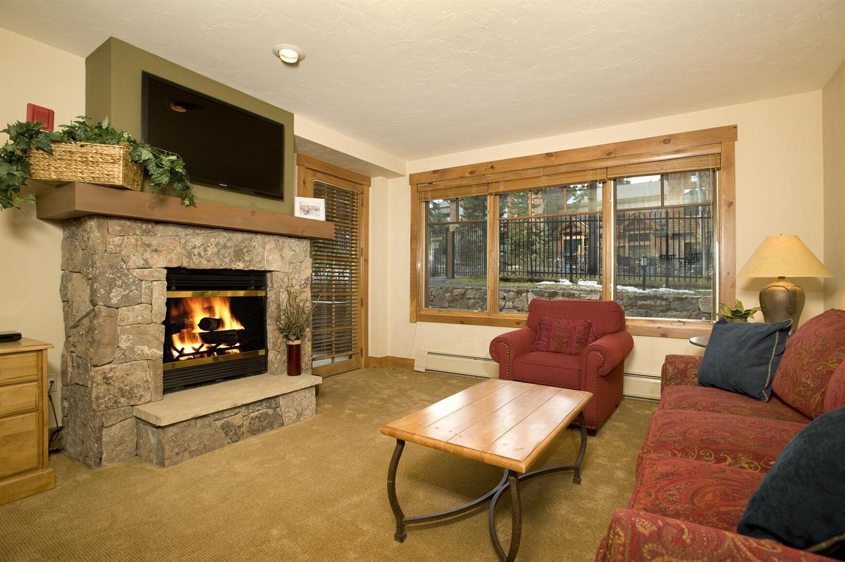 A living room with a stone fireplace, a red armchair, a wooden coffee table, and a sofa with patterned cushions.