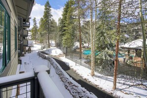 Un sendero cubierto de nieve que conduce a una zona de piscina, rodeada de árboles y un edificio con balcones.