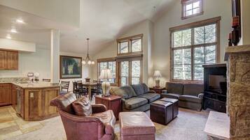 A spacious living room with a fireplace, large windows, and a kitchen area.