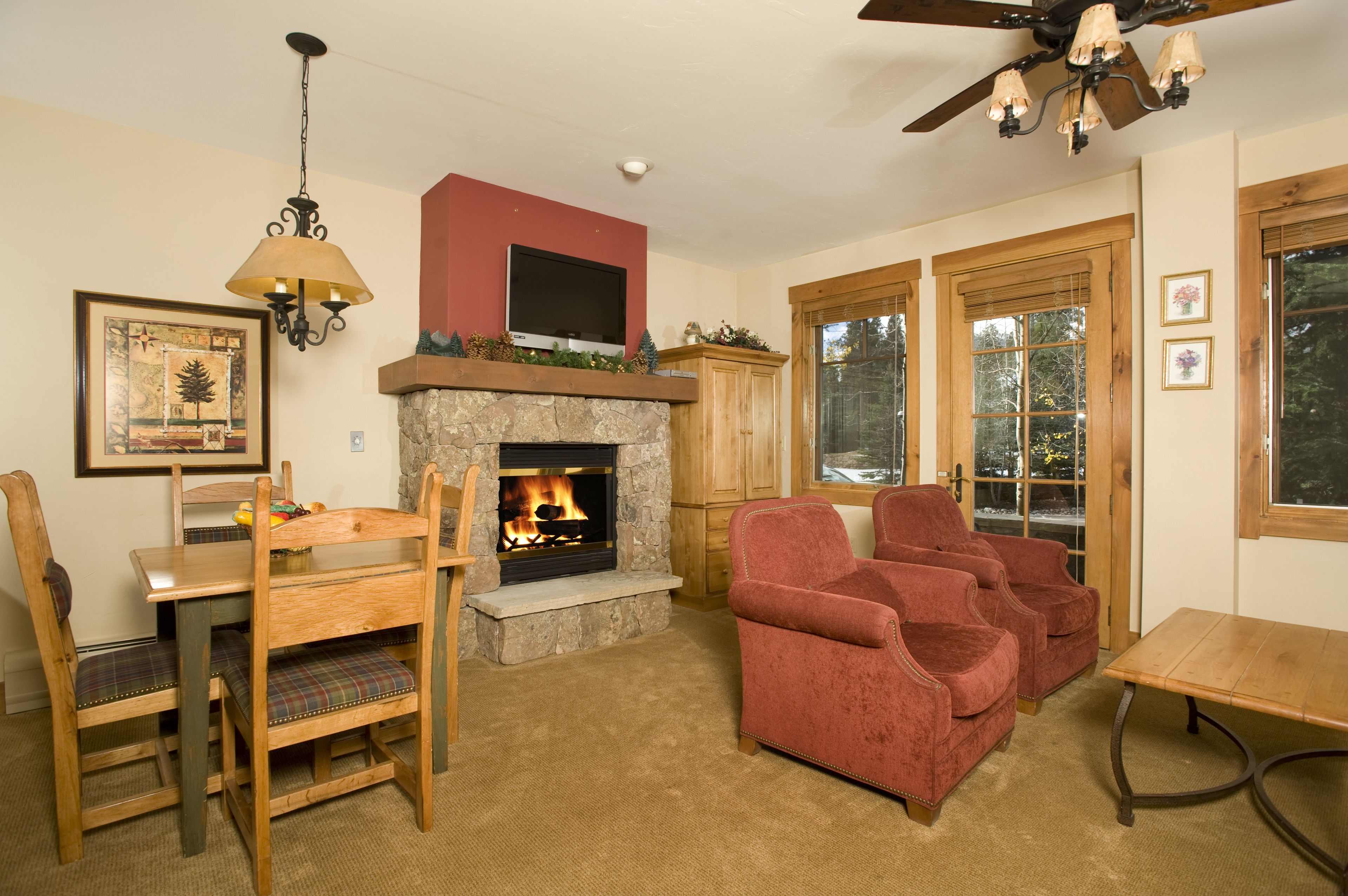 A cozy living room with a fireplace, wooden furniture, and a ceiling fan.