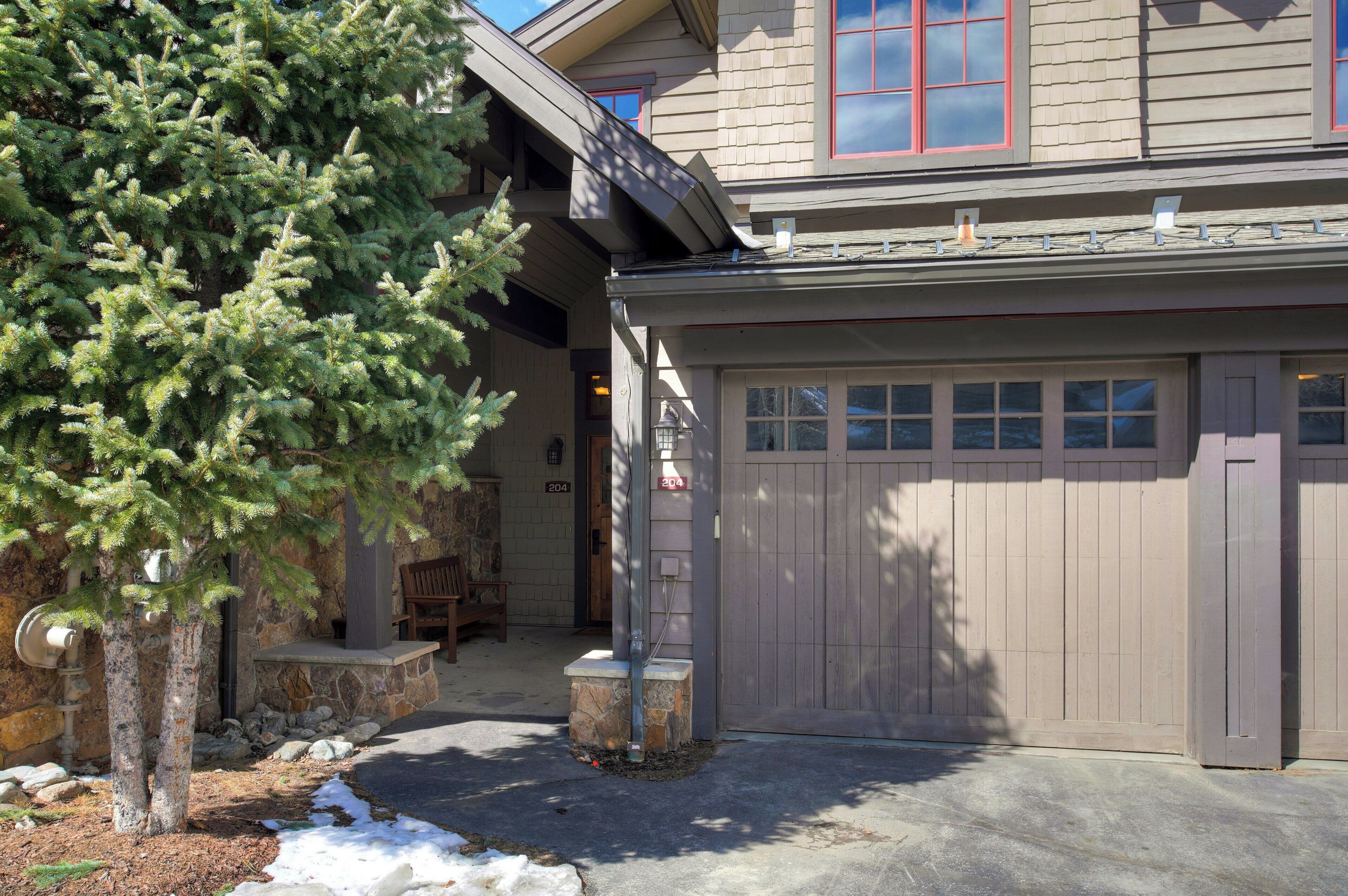 Une maison avec un garage, un pilier en pierre et un arbre.
