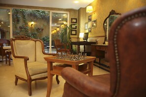 A room with a chess table, a wooden chair, and a desk with a lamp.