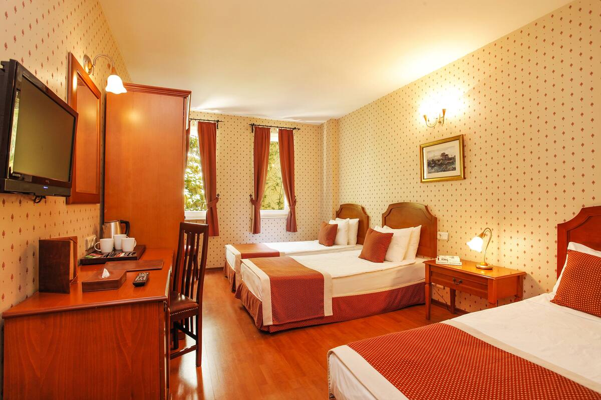 A hotel room with two beds, a desk, a television, and a window with curtains.