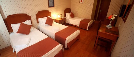 A hotel room with three single beds, a wooden desk, and a small table with a vase.