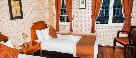 A hotel room with two beds, a wooden floor, a chair, and a window with curtains.