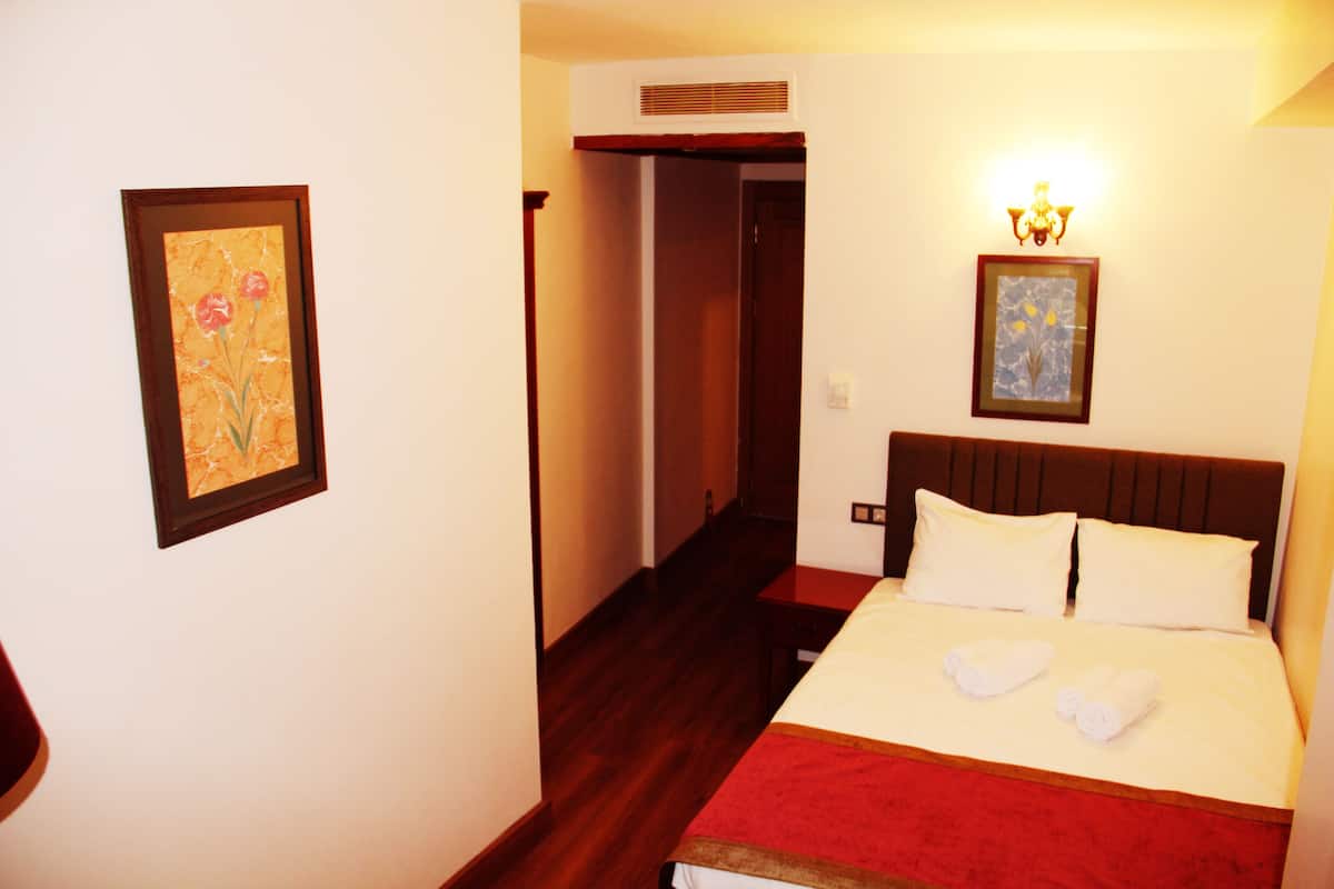 A hotel room with a bed, a nightstand, and a wall-mounted lamp.