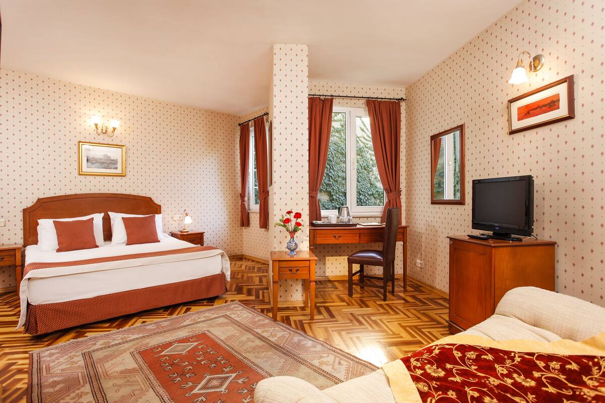 A hotel room with a bed, desk, chair, television, and a view of the outdoors.