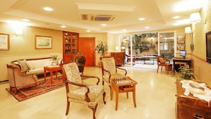 A spacious lobby with a sofa, armchairs, a chess table, and a reception desk.