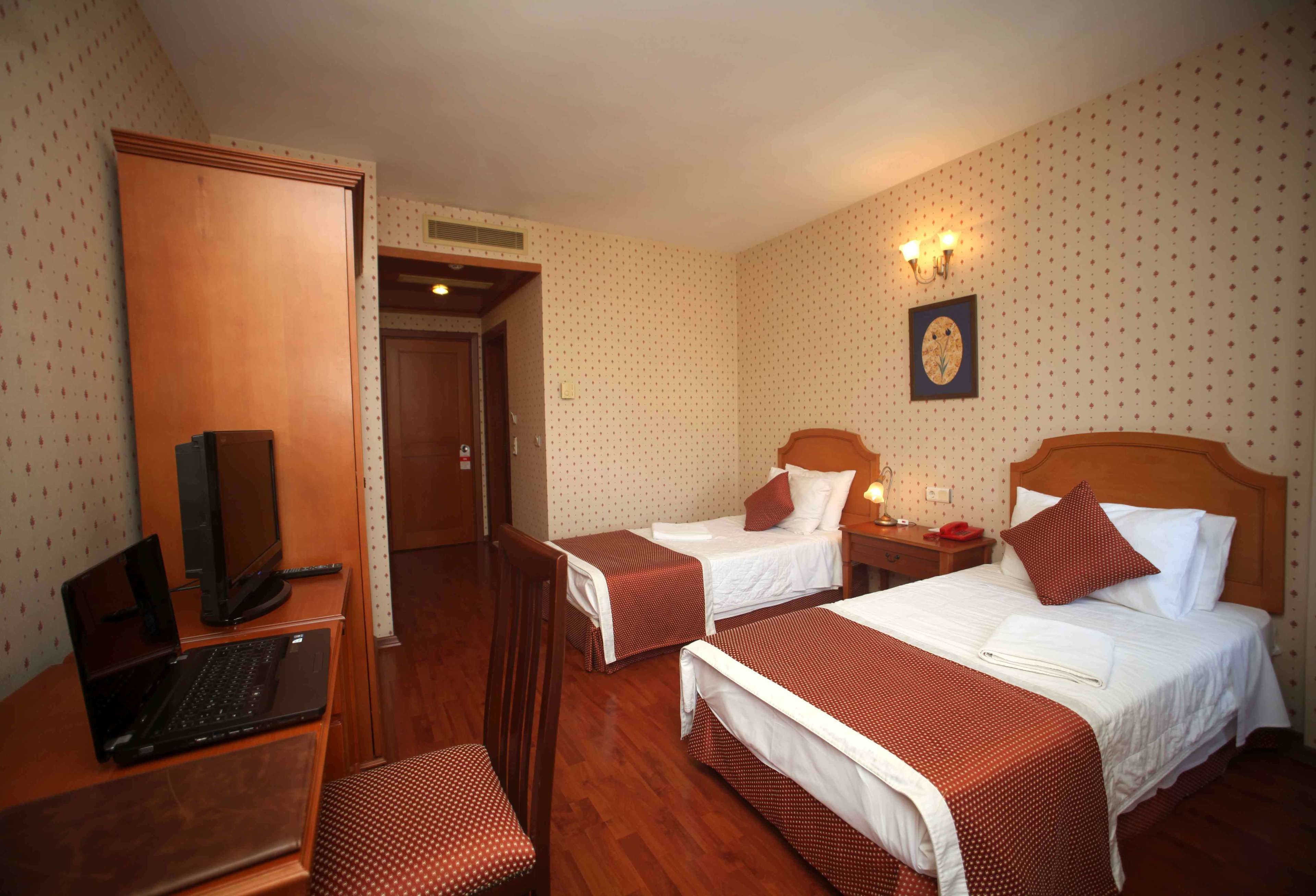 Une chambre d’hôtel avec deux lits, un bureau avec un ordinateur portable, une chaise et une armoire en bois.
