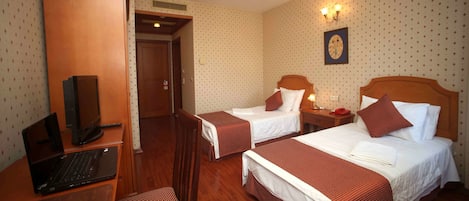 A hotel room with two beds, a desk with a laptop, a chair, and a wooden wardrobe.