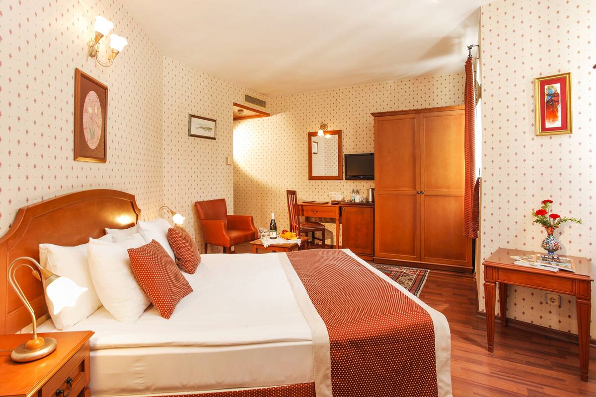 A hotel room with a large bed, a desk, a chair, and a wardrobe.