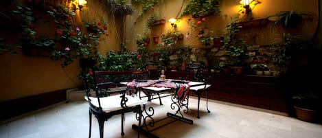 An indoor patio with a table and chairs, surrounded by potted plants and flowers, with wall-mounted lights.