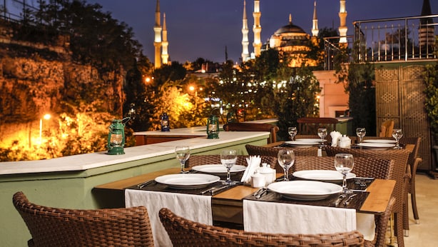 A dining area with tables set for a meal, overlooking a historic building with multiple minarets.