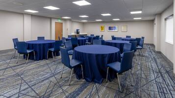 A conference room with multiple round tables covered with blue tablecloths, surrounded by blue chairs.