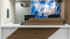 A reception desk with a modern design, featuring a blue geometric wall and a wooden accent. - Holiday Inn Express & Suites Center Township by IHG (Monaca)