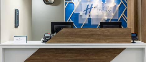 Un mostrador de recepción de diseño moderno, con un muro geométrico azul y un detalle de madera.
