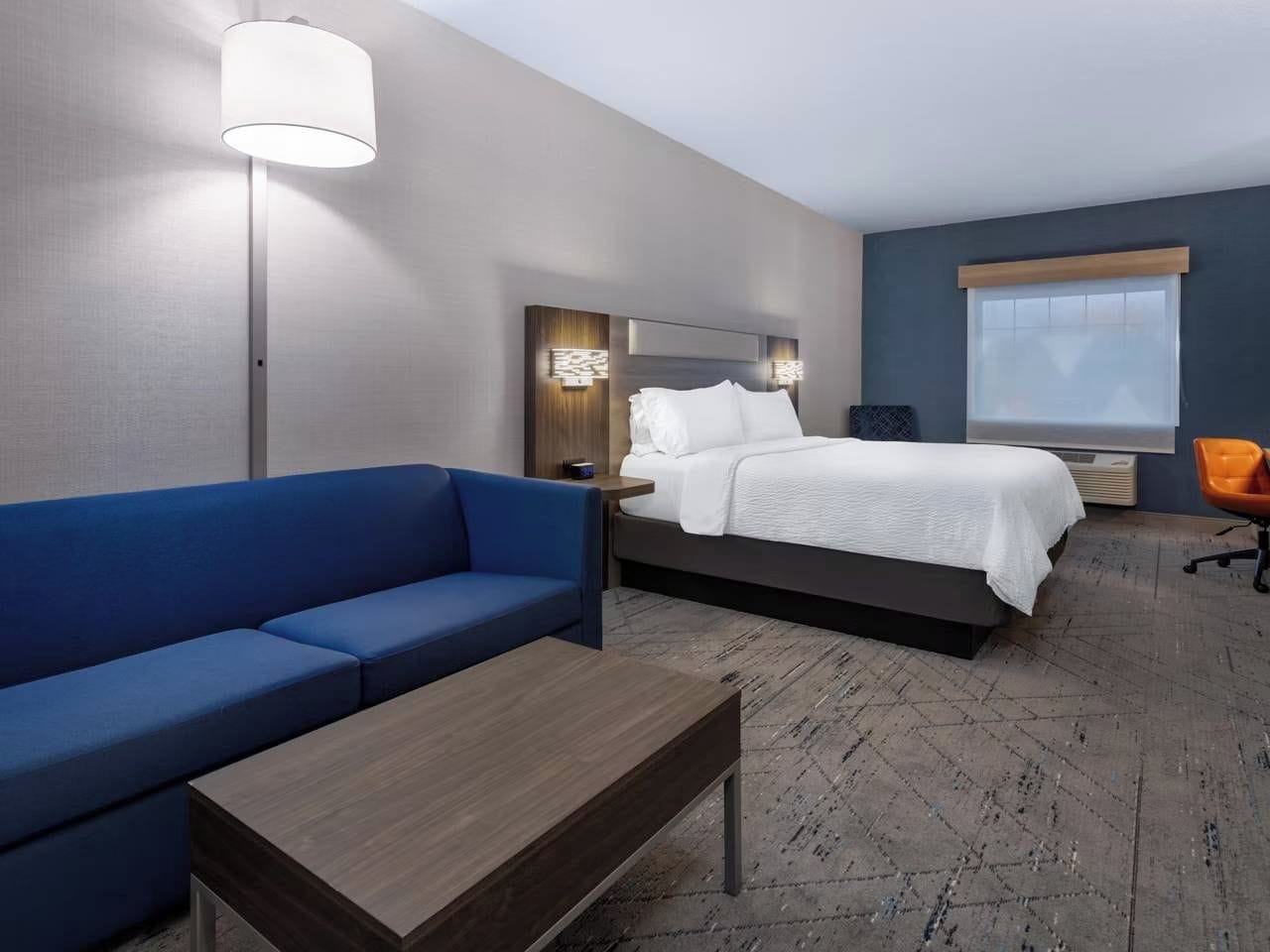 A hotel room with a bed, a blue sofa, a wooden coffee table, and a lamp.