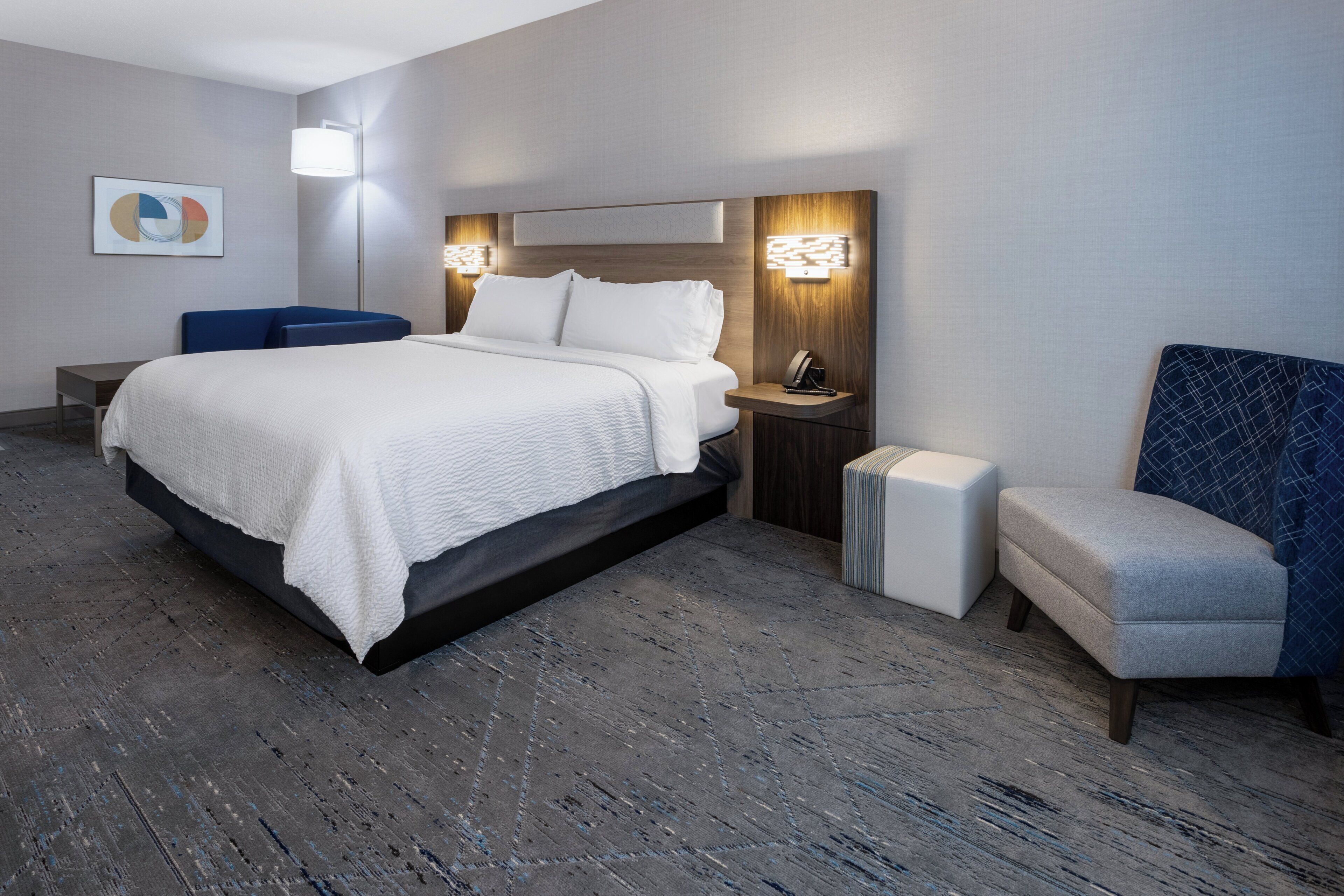 Una habitación de hotel con una cama, mesitas de noche, una silla y una lámpara de pared.