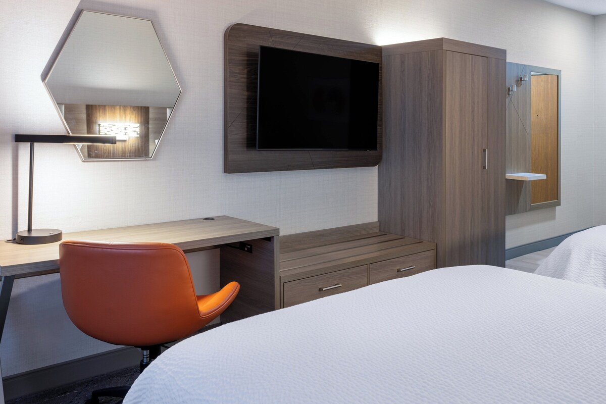 Ein Hotelzimmer mit einem Bett, einem Schreibtisch mit Stuhl, einem an der Wand montierten Fernseher und einem Kleiderschrank.
