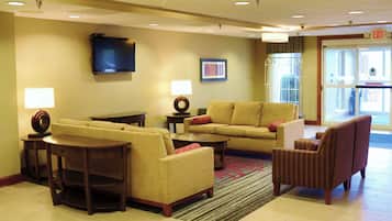 Um hall de hotel com um conjunto de sofás, uma televisão na parede e piso coberto de carpete.