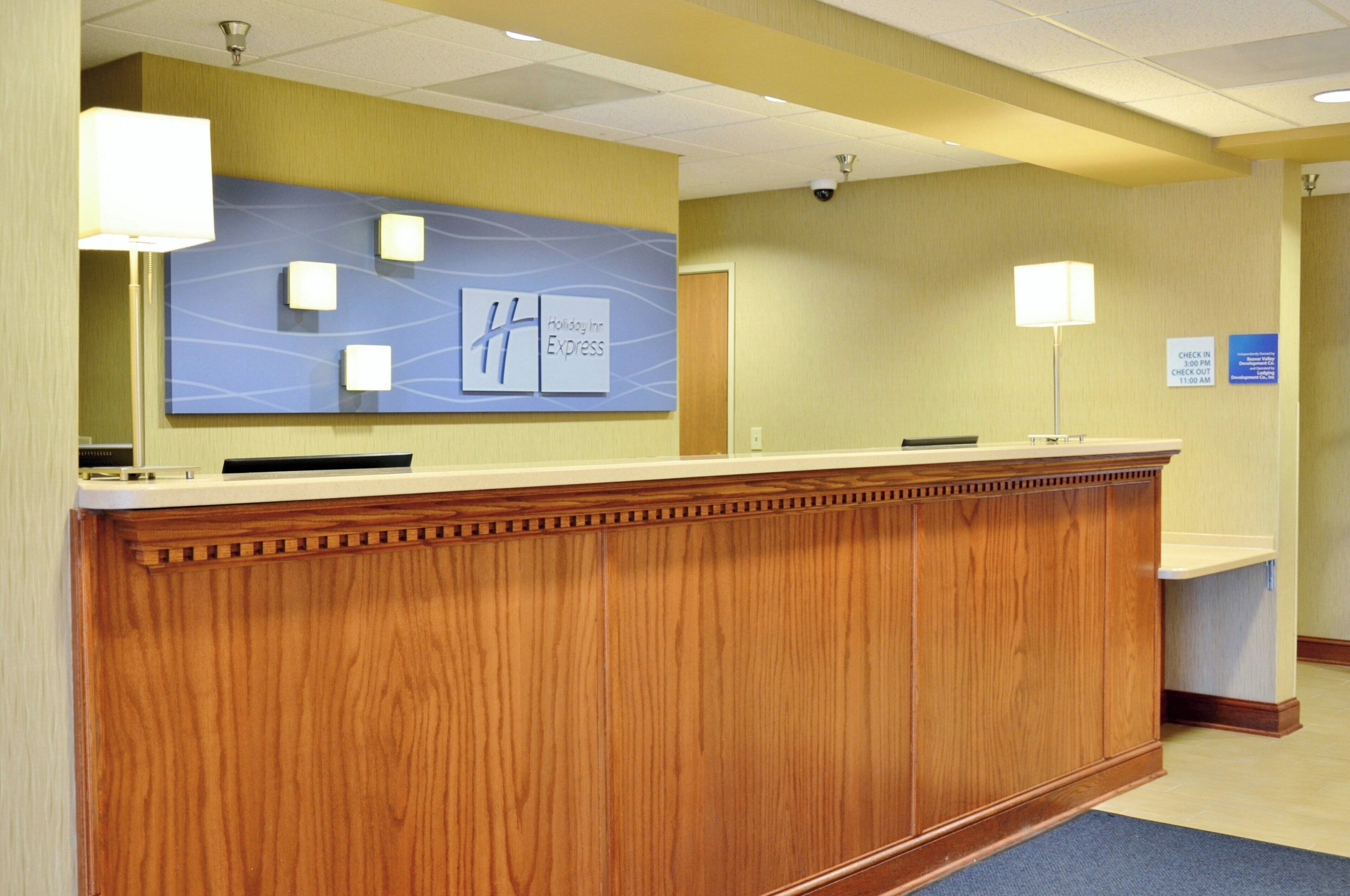 A reception desk with a wooden finish, a Holiday Inn Express sign above it, and a check-in/out sign on the wall to the right.