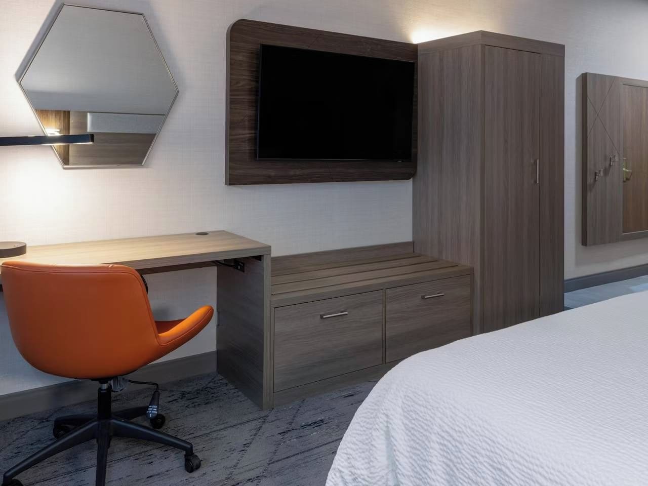 Une chambre d’hôtel comprenant un lit, un bureau avec une chaise, une armoire et un téléviseur fixé au mur.