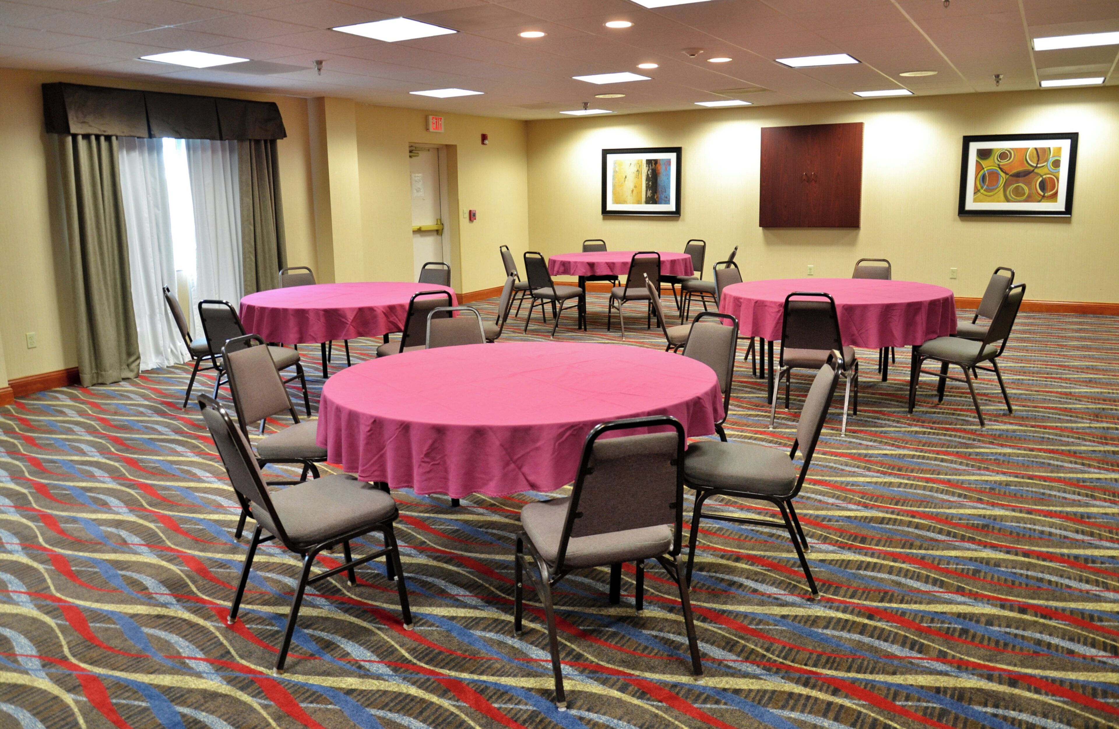 A conference room with multiple round tables, each covered with a pink tablecloth, surrounded by chairs.