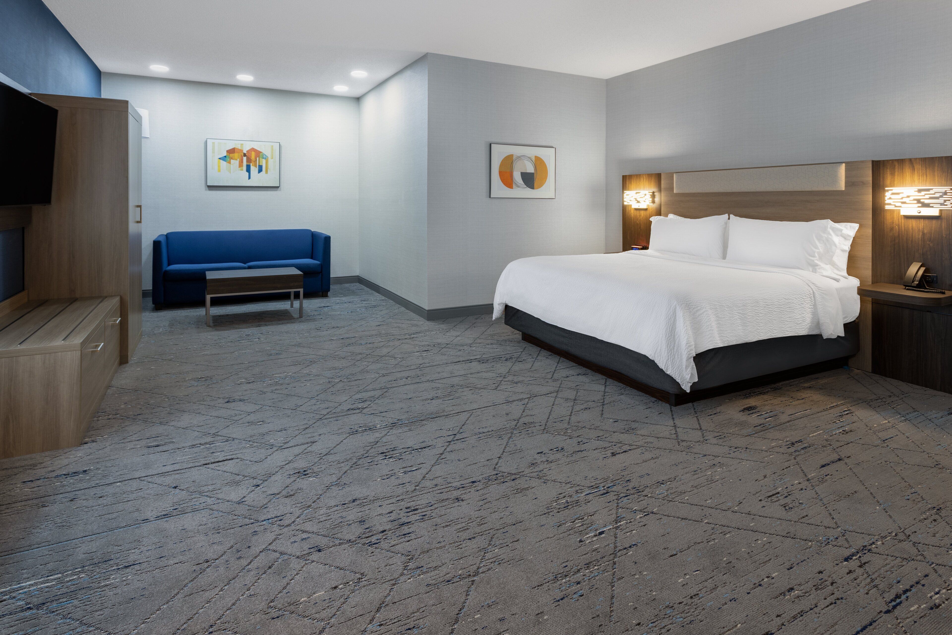 A modern hotel room with a large bed, a blue sofa, and a flat-screen TV.