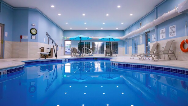 An indoor swimming pool with blue tiles, a clock on the wall, and lounge chairs by the pool. - Holiday Inn Express & Suites Center Township by IHG (Monaca)